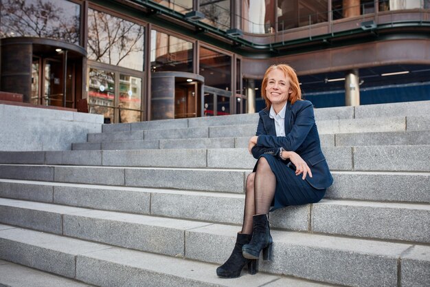 Confiada mujer de negocios de mediana edad tomando un merecido descanso del mundo de los negocios urbanos