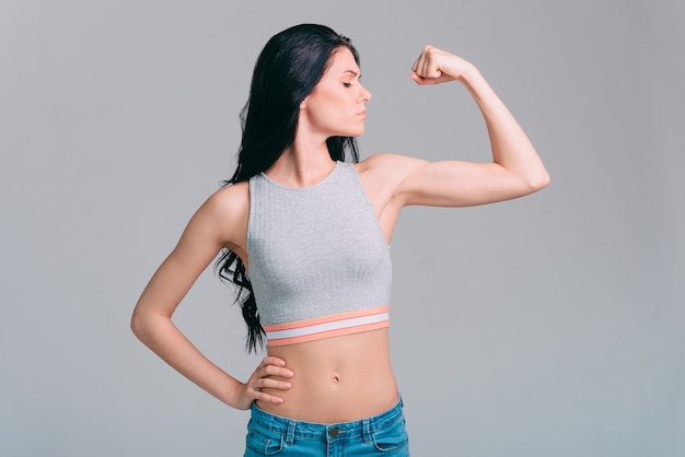 Confiada en su cuerpo perfecto. Atractiva joven mujer deportiva mirando sus bíceps mientras está de pie