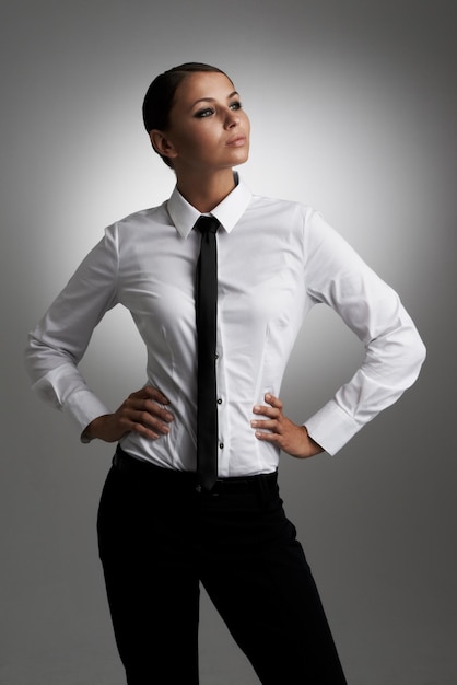 Confiada en su estilo Una mujer joven con camisa y corbata mirando de lado con las manos en las caderas