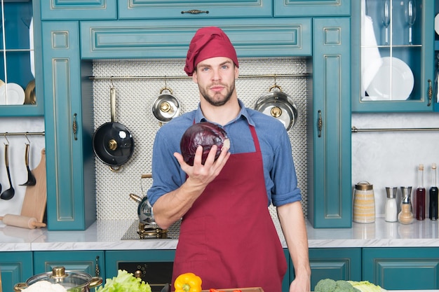 Confiado en la cocina Tome viejos favoritos y haga sustituciones saludables Tome recetas favoritas y aligerarlas Hombre apuesto chef sostiene repollo violeta pensando qué plato saludable cocinar