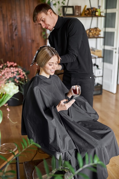 Confiado estilista masculino está teñiendo el cabello de una clienta caucásica rubia