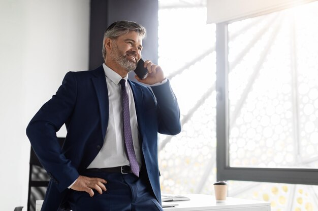 Confiado hombre de negocios de mediana edad en traje hablando por teléfono celular en la oficina