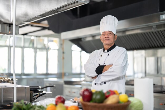 Foto confiado jefe de cocina asiático en vestido blanco de pie y brazos cruzados en el restaurante de la cocina