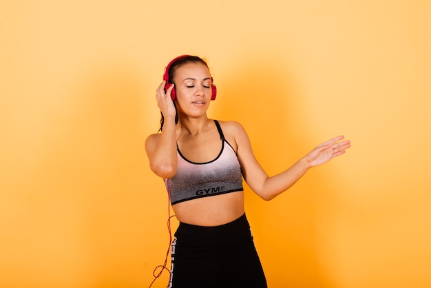 Confiado joven deportista africana en forma escuchando música con auriculares sobre fondo amarillo