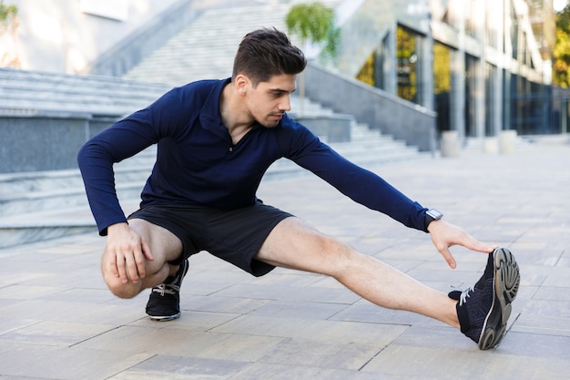 Confiado joven deportista haciendo ejercicios de estiramiento al aire libre