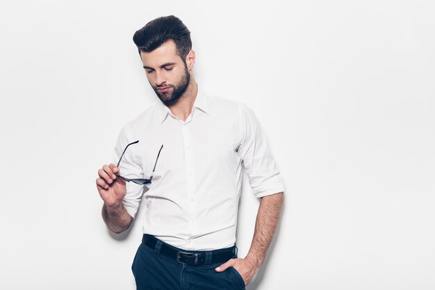 Confiado en su estilo. Apuesto joven con camisa blanca sosteniendo gafas de sol y mirándolos