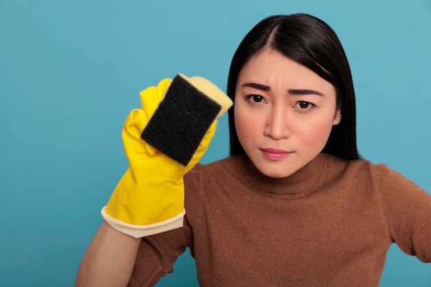 Confiança séria jovem dona de casa asiática usando luvas amarelas segurando uma esponja, trabalhadora dona de casa, conceito de limpeza em casa, dona de casa fiel cansada e sobrecarregada de tarefas do dia a dia