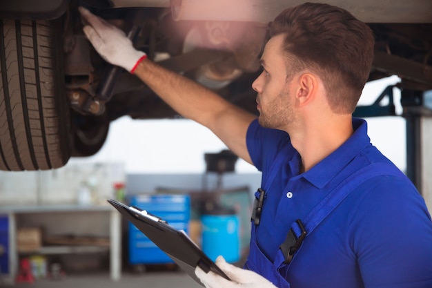 Foto confiante e concentrado, jovem e experiente especialista em reparos automotivos com um tablet na mão, inspeciona e diagnostica o carro em busca de avarias