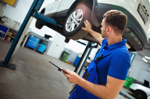 Confiante e concentrado, jovem e experiente especialista em reparos automotivos com um tablet na mão, inspeciona e diagnostica o carro em busca de avarias
