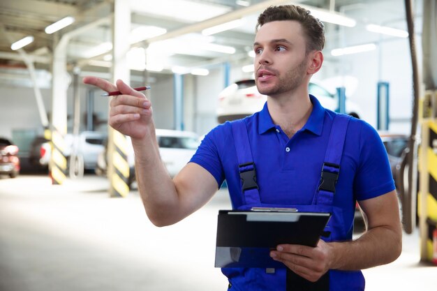 Confiante e concentrado, jovem e experiente especialista em reparos automotivos com um tablet na mão, inspeciona e diagnostica o carro em busca de avarias