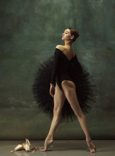 Foto confiante. graciosa bailarina clássica dançando, posando isolada no fundo escuro do estúdio. elegance tutu preto. conceito de graça, movimento, ação e movimento. parece leve, flexível. elegante.