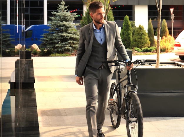 Confiante jovem empresário andando com bicicleta na rua da cidade