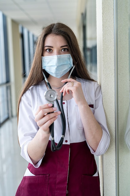 Confiante jovem médica feliz mostrando luta contra o vírus da doença usando máscara e luvas