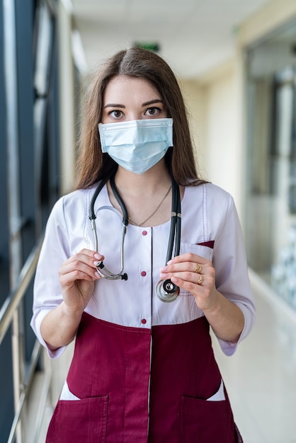 Confiante jovem médica feliz mostrando luta contra o vírus da doença usando máscara e luvas