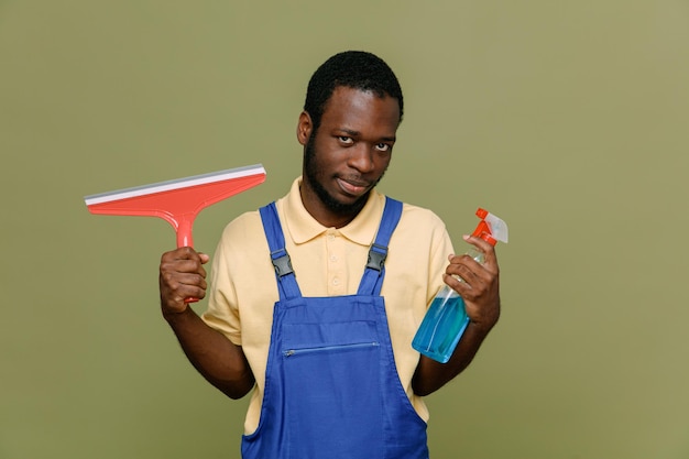 Confiante segurando o esfregão com agente de limpeza jovem limpador afro-americano de uniforme com luvas isoladas em fundo verde