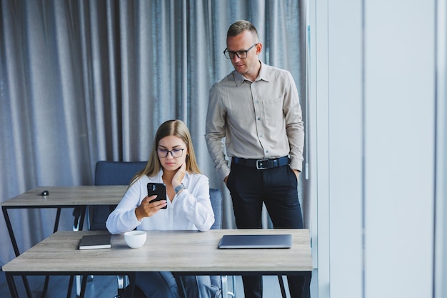 Confiantes colegas homens e mulheres em roupas casuais elegantes estão discutindo um projeto no local de trabalho desfrutando de amizade corporativa parceiros felizes estão falando sobre redes de escritório em um telefone celular