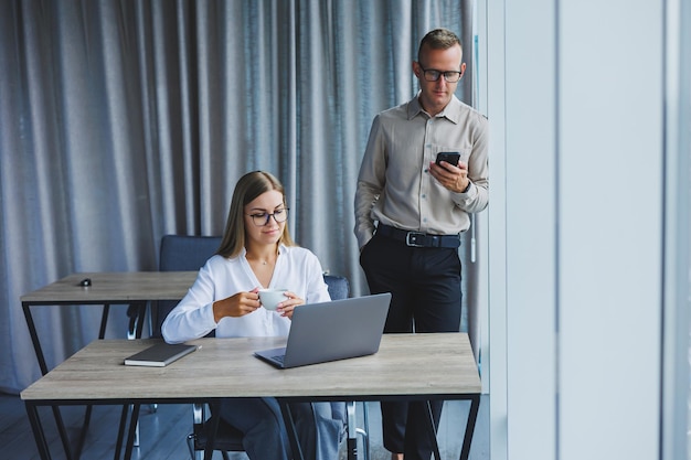 Confiantes colegas homens e mulheres em roupas casuais elegantes estão discutindo um projeto no local de trabalho desfrutando de amizade corporativa parceiros felizes estão falando sobre redes de escritório em um telefone celular