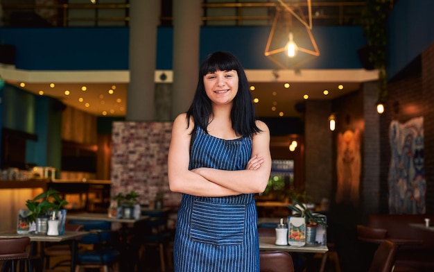 Con confianza a cargo de servir a los clientes Foto de una camarera de pie en la entrada de un bar