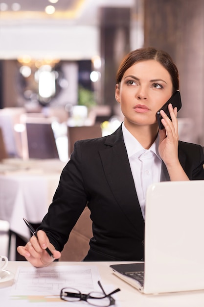 Foto confianza empresaria. mujer joven pensativa en ropa formal hablando por teléfono y mirando a otro lado mientras está sentado en el restaurante