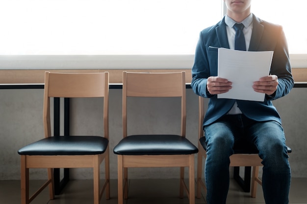 Confianza joven empresario sosteniendo el papel mientras está sentado en una fila de sillas, esperando la entrevista.