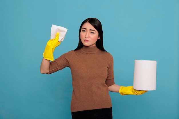 Confianza mujer joven con papel tisú sosteniendo en el guante amarillo de pie contra un fondo azul, concepto de hogar de limpieza, fiel mujer satisfecha de las tareas del día a día