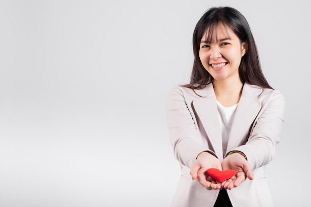 Confianza de mujer sonriente que muestra sostener el corazón rojo con la palma de la mano aislado fondo blanco, retrato asiático feliz hermosa joven mujer enviar amor y feliz San Valentín en foto de estudio, espacio de copia