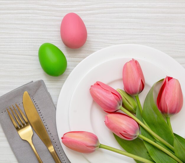 Configuração da mesa de Páscoa Cor de ovo pastel e tulipa rosa e talheres dourados em madeira branca acima da cabeça