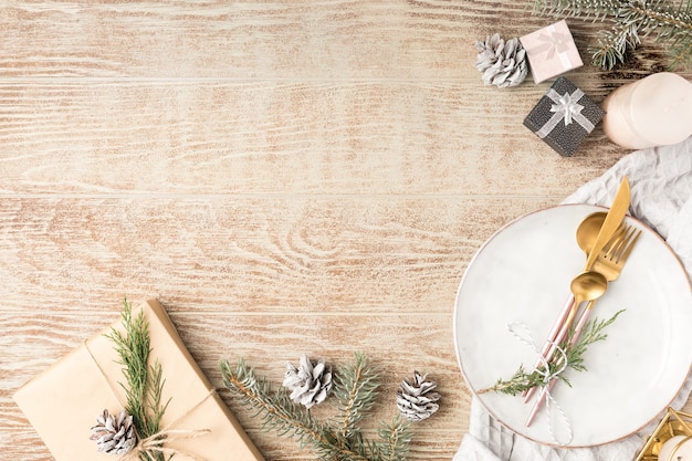 Configuração de mesa de madeira festiva com decorações de inverno, talheres, velas e presentes. Vista superior, configuração plana. O conceito de um jantar de Natal em família.