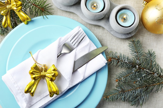 Configuração de mesa de Natal em cores azuis, douradas e brancas sobre fundo cinza de toalha de mesa