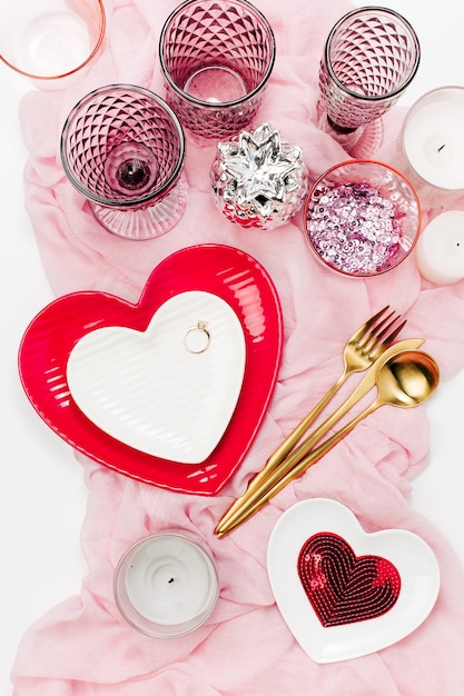 Foto configuração de mesa festiva. pratos brancos e vermelhos em forma de coração, copos para bebidas, velas e talheres de fundo branco. dia dos namorados ou conceito de casamento