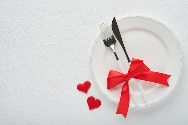 Configuração de mesa romântica do dia dos namorados Vazio ou closeup de um garfo de faca de prato preto de jantar e corações de seda decorativos em fundo branco Conceito de férias Copie o espaço para inscrições