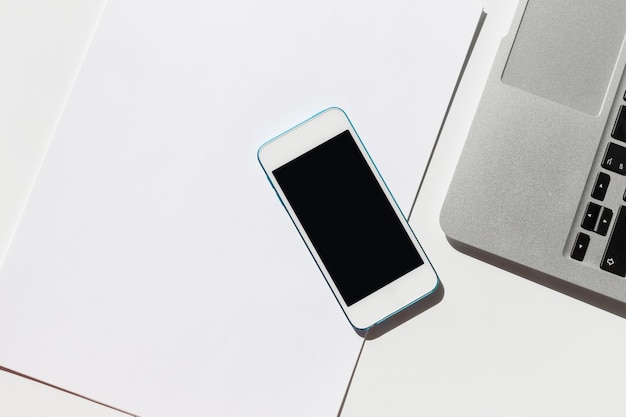 Configuración de escritorio de trabajo con un teléfono inteligente y una computadora portátil en un fondo blanco minimalista