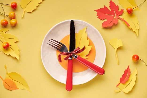 Configuración de la mesa para la celebración de otoño. Plato de cerámica sobre papel amarillo con papel Hojas de otoño