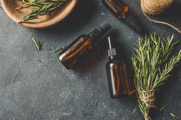 Configuración natural de bricolaje con botellas de spray de vidrio ámbar, hilo y romero fresco en un fondo rústico de textura negra, elementos ecológicos y orgánicos para el cuidado de la piel o la inspiración para la artesanía en el hogar.