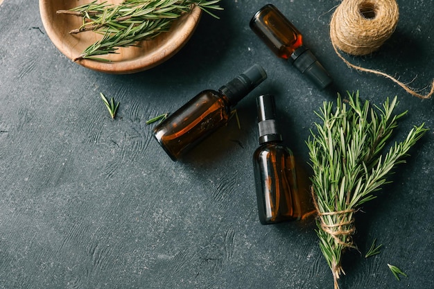 Configuración natural de bricolaje con botellas de spray de vidrio ámbar, hilo y romero fresco en un fondo rústico de textura negra, elementos ecológicos y orgánicos para el cuidado de la piel o la inspiración para la artesanía en el hogar.
