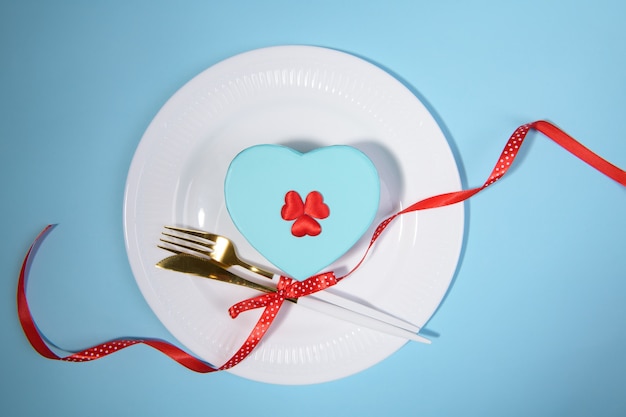 Configuración de la tabla de San Valentín regalo en un plato con cinta roja sobre fondo azul.