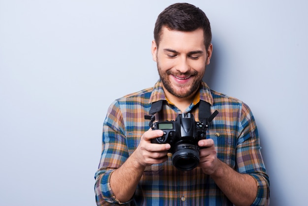 Configurando a câmera. Retrato de jovem confiante em uma camisa segurando a câmera em pé contra um fundo cinza