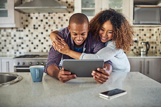 Confira esta foto recortada de um jovem casal afetuoso usando um tablet em sua cozinha em casa