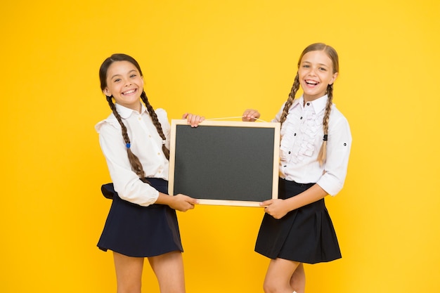 Confira isto alunos bonitos das meninas da escola seguram o espaço da cópia do quadro-negro conceito de anúncio da escola equipe de iniciativa dos colegas fundo amarelo junte-se ao clube da escola comunidade dos alunos horário escolar