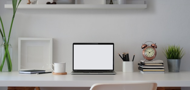 Confortável espaço de trabalho com laptop de tela aberta em branco e moldura com material de escritório