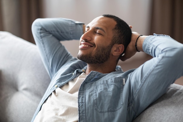 Conforto doméstico relaxado jovem negro recostado no sofá em casa