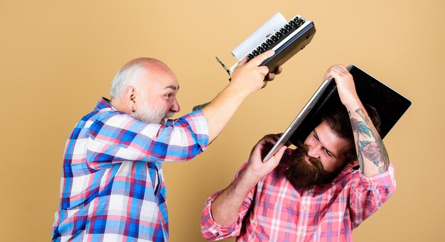 Confrontación batalla tecnológica Vida moderna juventud vs vejez enfoque empresarial padre e hijo generación familiar dos hombres barbudos Máquina de escribir vintage máquina de escribir retro vs portátil Nueva tecnología