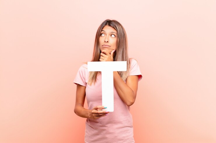 Foto confundido, dudoso, pensando, sosteniendo la letra t del alfabeto para formar una palabra o una oración.