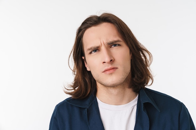 Confundido guapo con cabello largo mirando hacia arriba y pensando aislado sobre la pared blanca