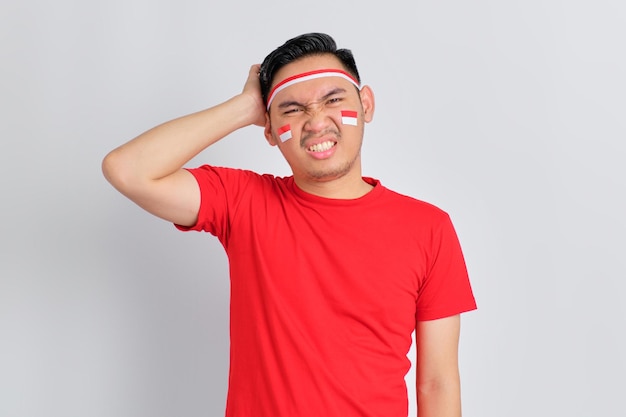 Confundido joven asiático celebrando el día de la independencia de Indonesia rascándose la cabeza con la cara perpleja aislado sobre fondo blanco.