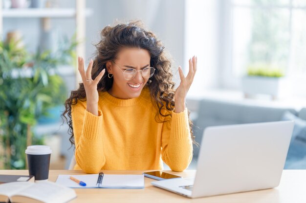 Confusa e frustrada jovem empresária estudando online, assistindo webinar, podcast no laptop, fazendo anotações, sentado na mesa de trabalho.