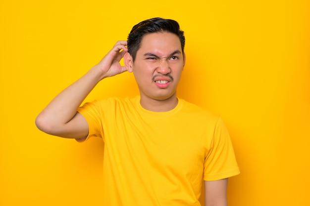 Confuso jovem asiático em camiseta casual tocando sua cabeça com a mão tendo problema isolado em fundo amarelo Conceito de estilo de vida de pessoas