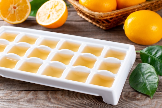 Congelando suco de limão em cubos em uma bandeja com limões frescos em uma mesa de madeira
