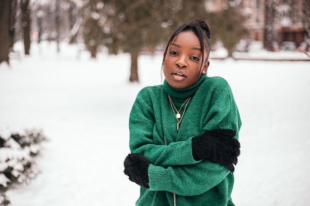 Congelante mulher afro-americana em pé na rua com fundo de neve branca