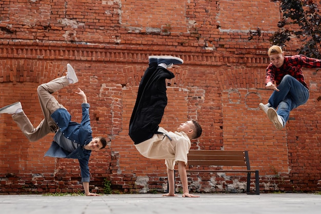 Congelar el marco de todo el equipo de breakdance masculino saltando en el aire contra la pared de ladrillo al aire libre